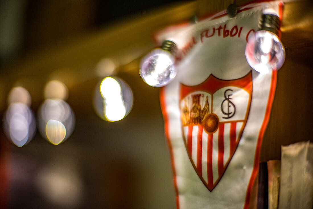 Ein unscharfes Bild eines Banners des FC Sevilla, beleuchtet von festlichen Lichterketten. Ideal für Feierlichkeiten und sportbezogene Bilder.