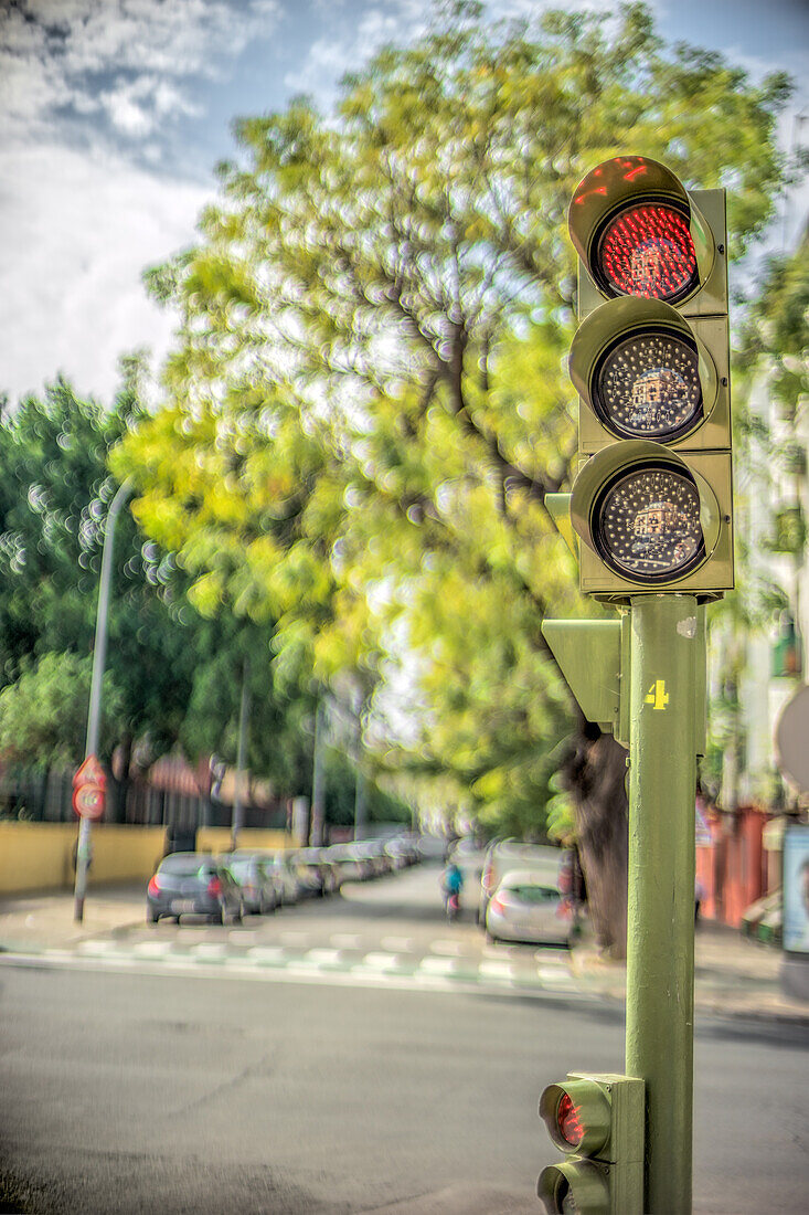 Red traffic light on a quiet, tree-lined street in Sevilla, España. Perfect for urban travel and city concepts.