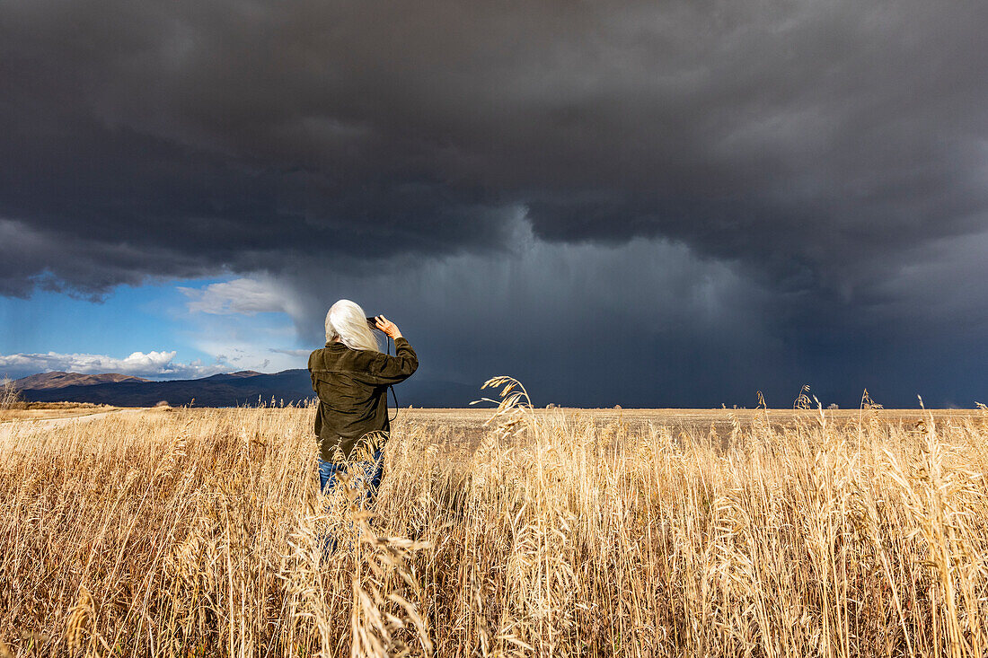 Rear view of woman taking photo of approaching storm with smart phone