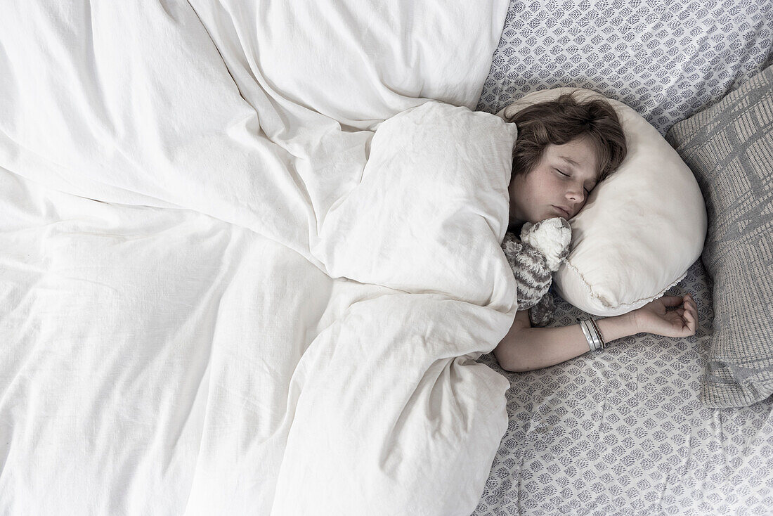 Draufsicht auf einen Jungen, der mit einem Stofftier im Bett schläft