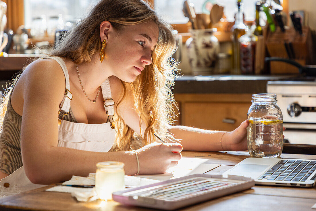 Teenagerin malt mit Aquarellfarben am Tisch