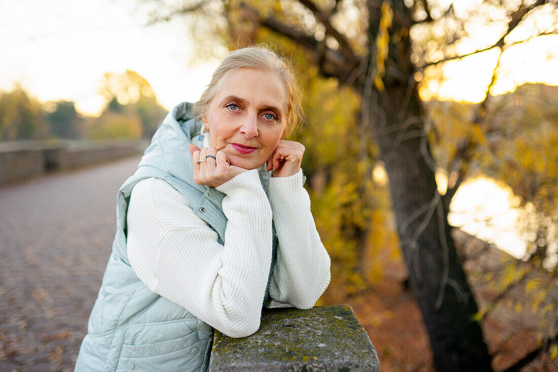 Porträt einer Frau, die sich im Herbst an eine Mauer am Fluss lehnt