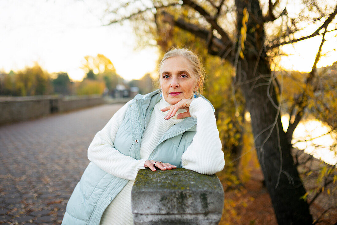 Porträt einer Frau, die sich im Herbst an eine Mauer am Fluss lehnt