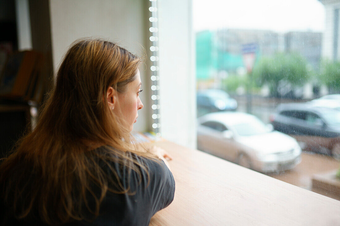 Frau lehnt auf der Fensterbank und schaut durch das Fenster