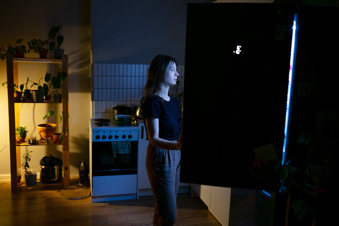 Woman standing in front of open refrigerator at night