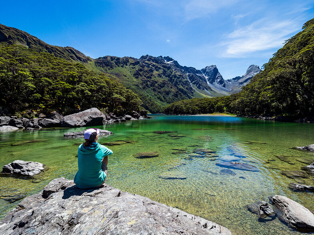 Rear view of woman sitting on lakeshore in Fiordland National Park