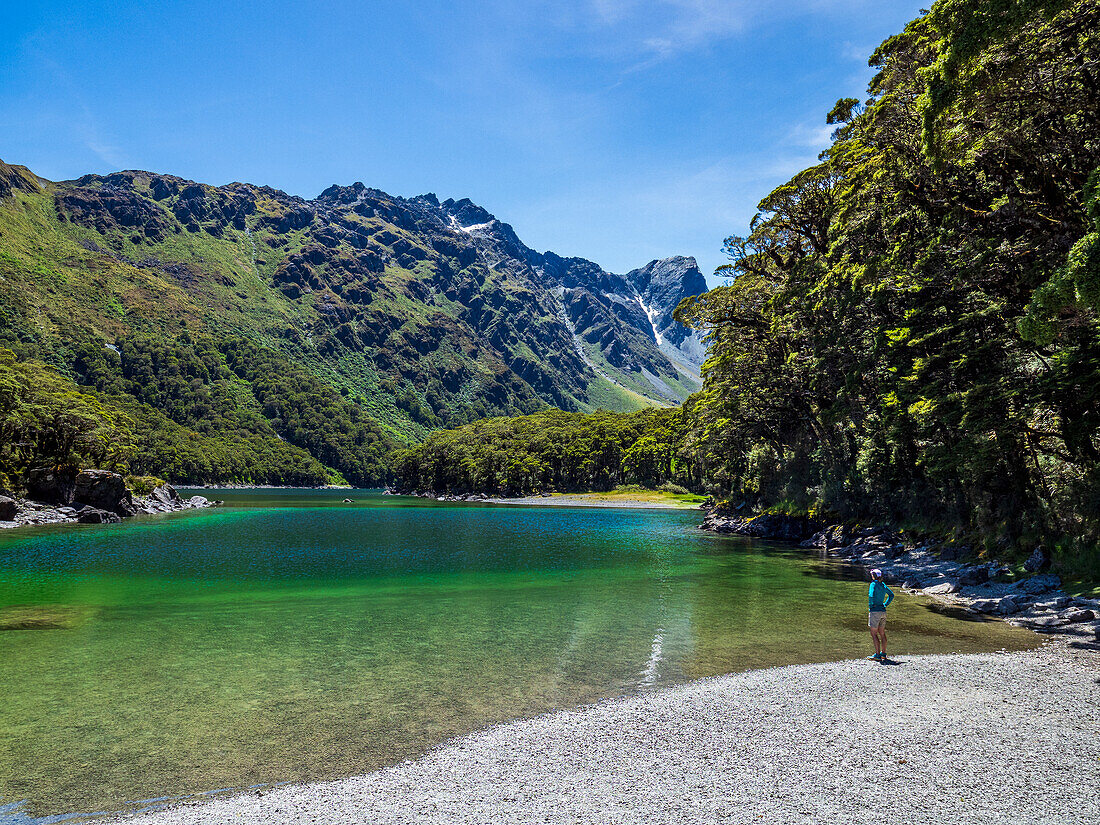 Rückansicht einer Frau, die am Seeufer im Fiordland-Nationalpark sitzt