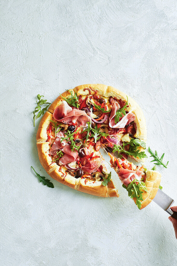 Pizza mit Prosciutto, Rucola, Zwiebeln und Oliven