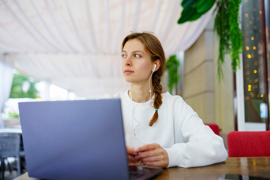 Frau mit Kopfhörern und Laptop am Cafétisch