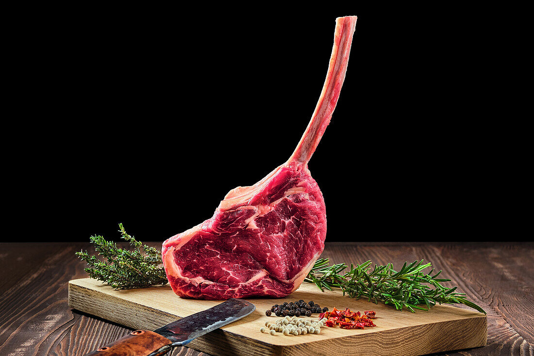 Raw tomahawk steak on a cutting board with spices and herbs