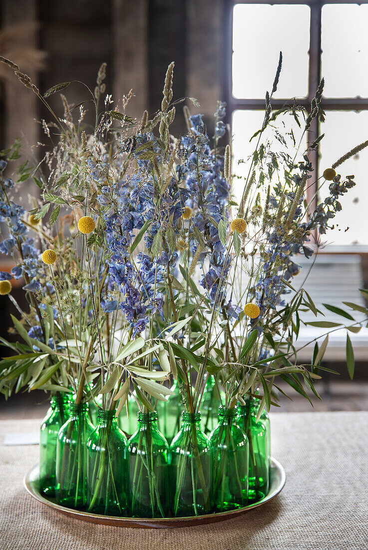 Getrocknete Wiesenblumen in grünen Glasflaschen auf rundem Tablett