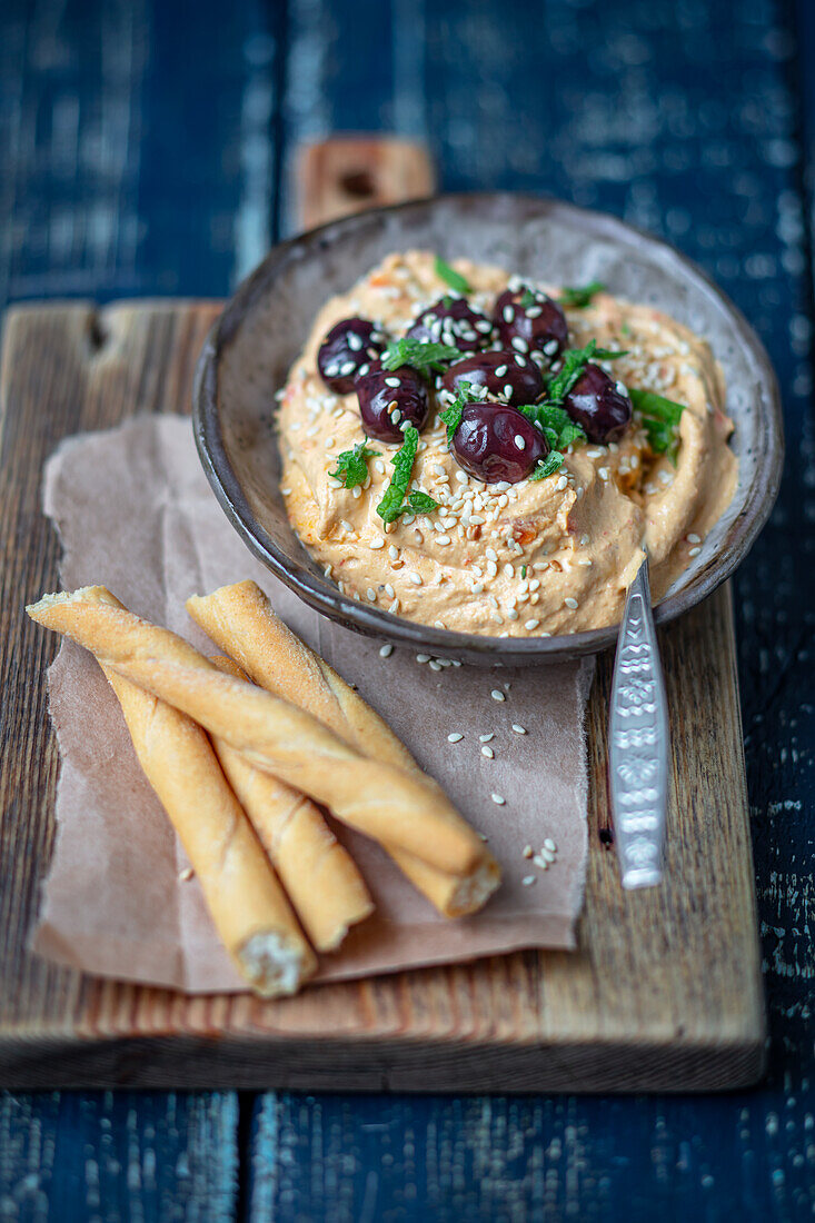 Paprika-Hummus mit Oliven und Brotstangen