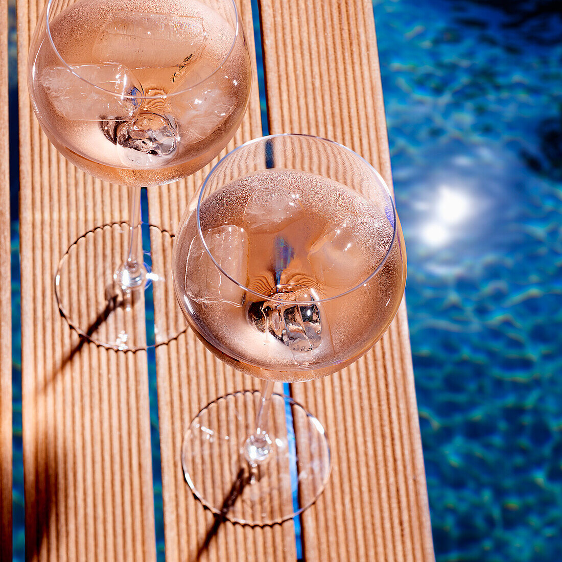 Glasses of rosé wine on a jetty by the pool