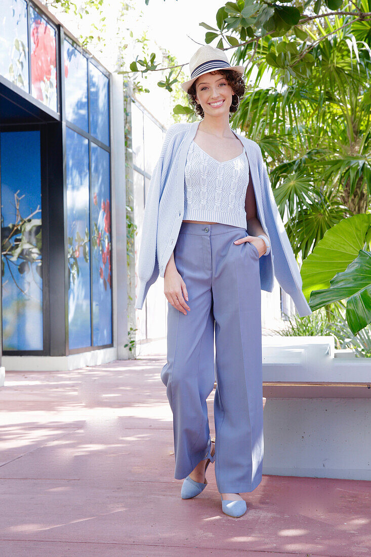 Young woman in casual business outfit walking outside with straw hat