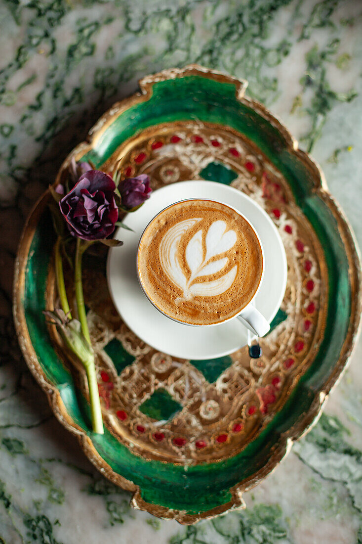 Cappuccino mit Latte Art dekoriert mit roter Blume auf Tablett