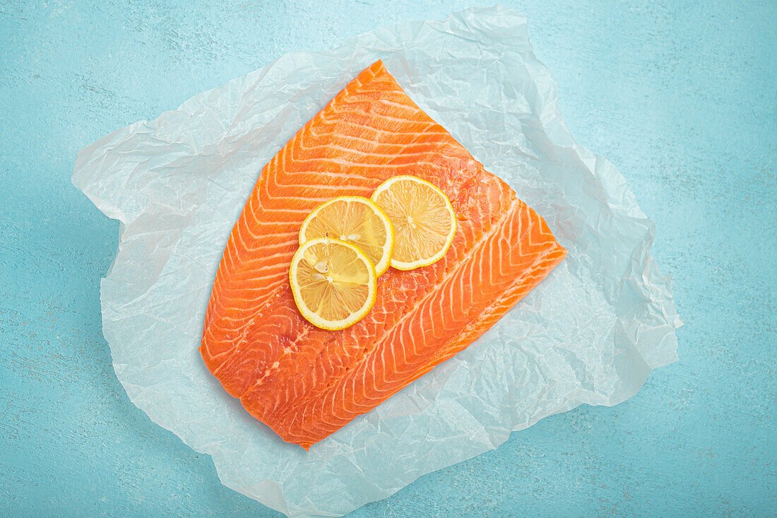 Fresh salmon fillet with lemon slices on a light blue background