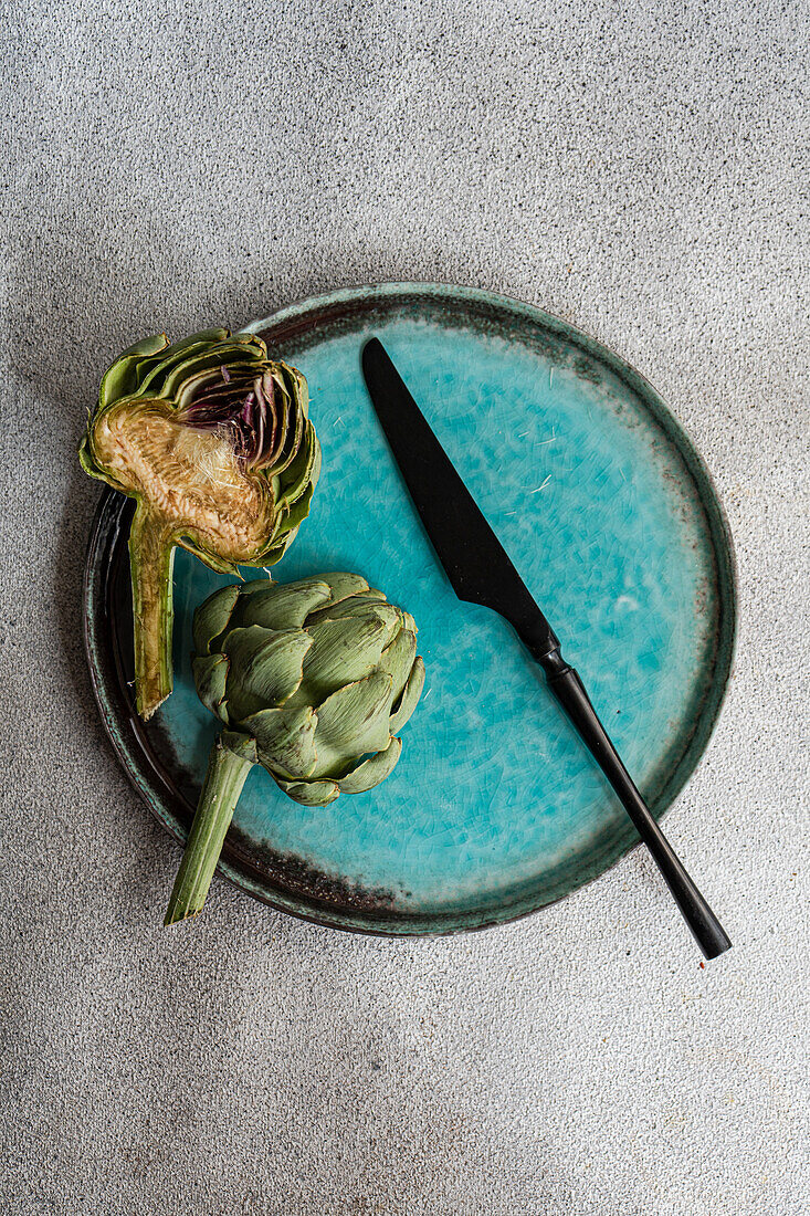 Halved raw artichoke and knife on a turquoise plate