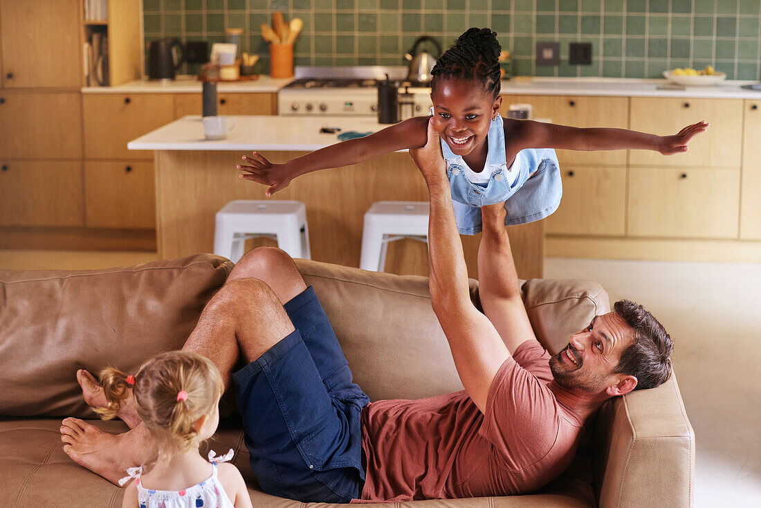 Father playing with daughters on sofa