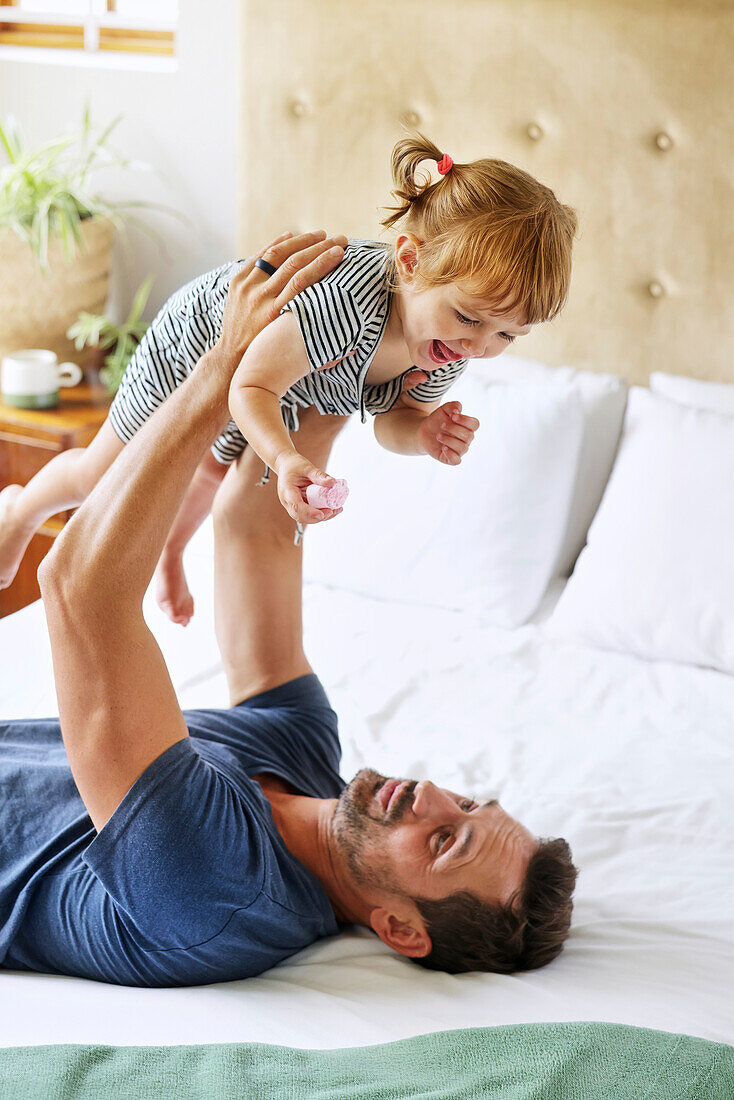 Father playing with daughter on bed