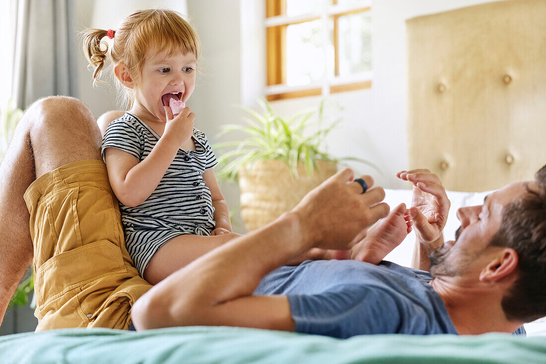 Father playing with daughter on bed