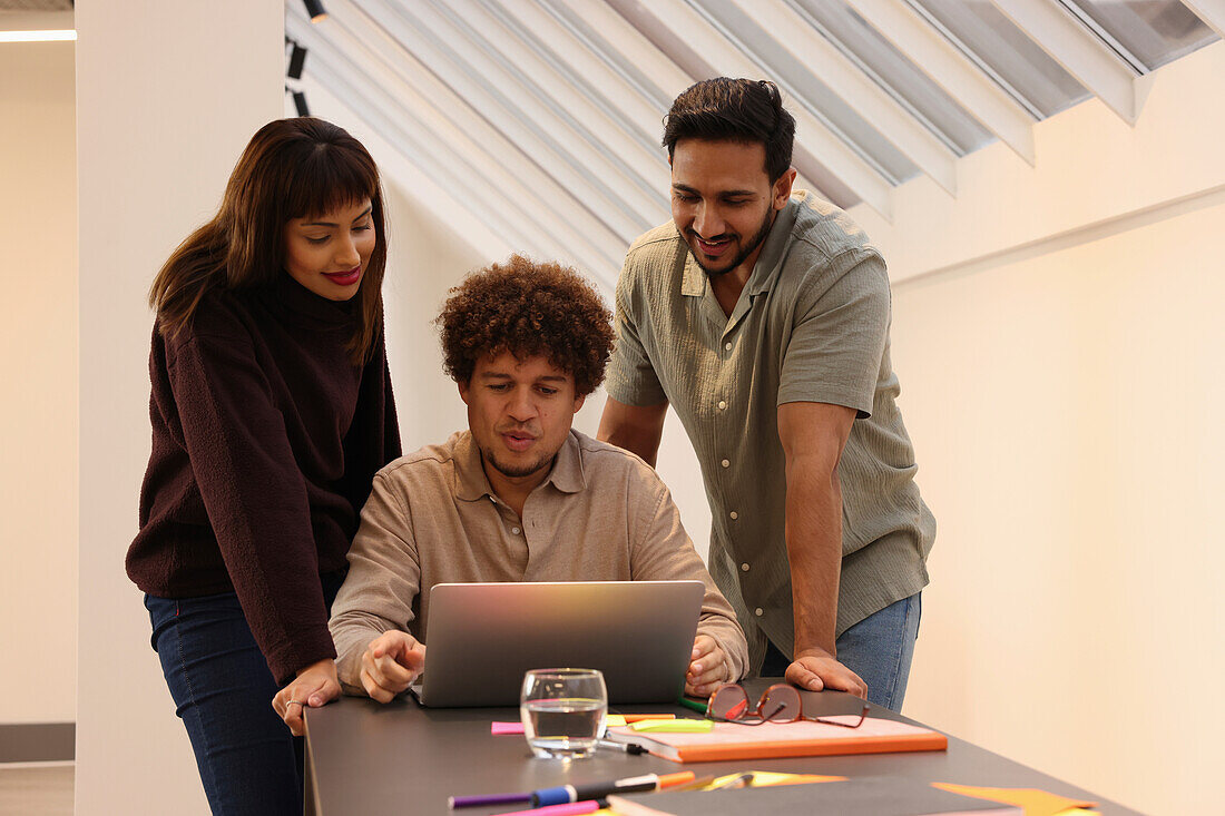 Coworkers looking at laptop at table in office