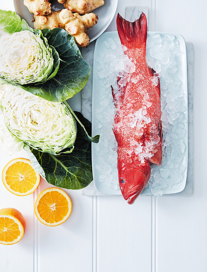 Red coral fish on ice with cabbage, Jerusalem artichokes and oranges