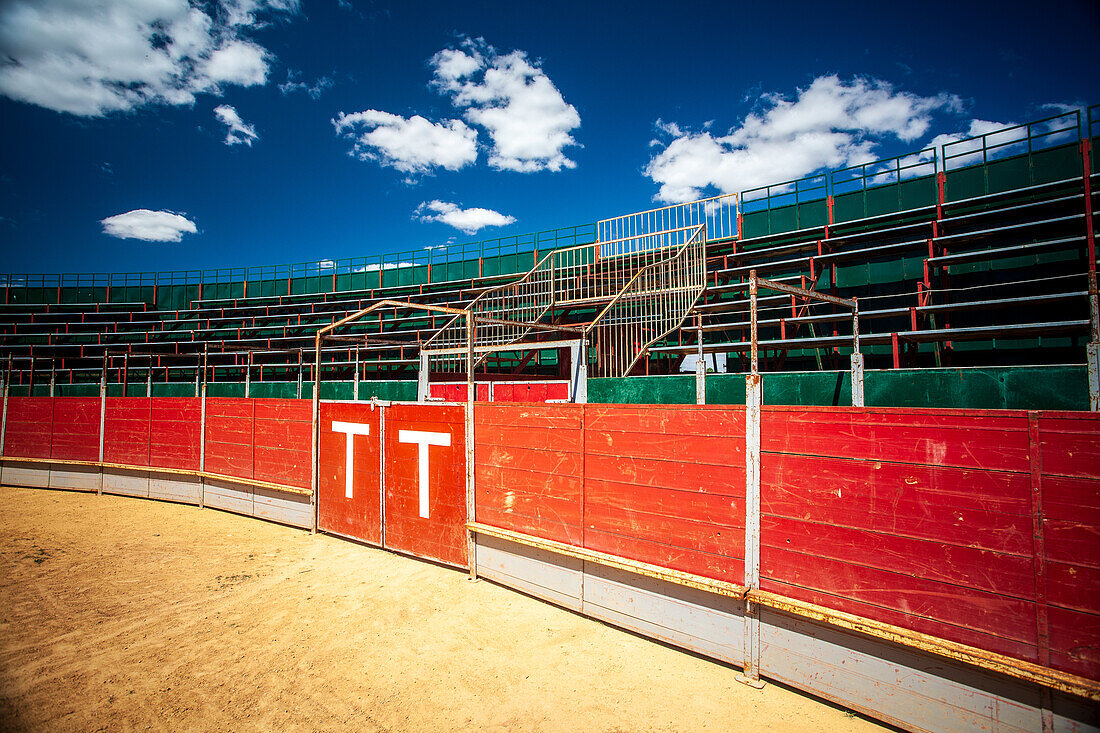 A scenic view of an empty portable bullring in Aznalcazar, Sevilla, Spain, showcasing vibrant colors under a clear blue sky.