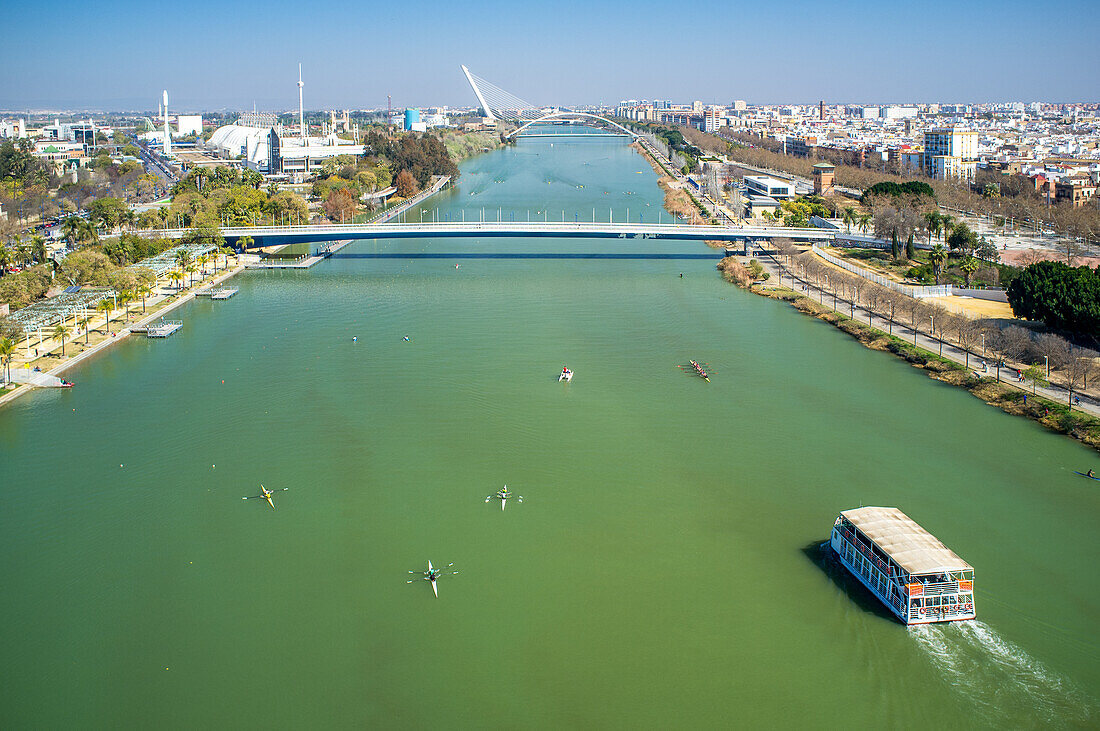 Aerial view of the Guadalquivir River with boats and the cityscape of Seville, highlighting the vibrant atmosphere and beautiful landscape.