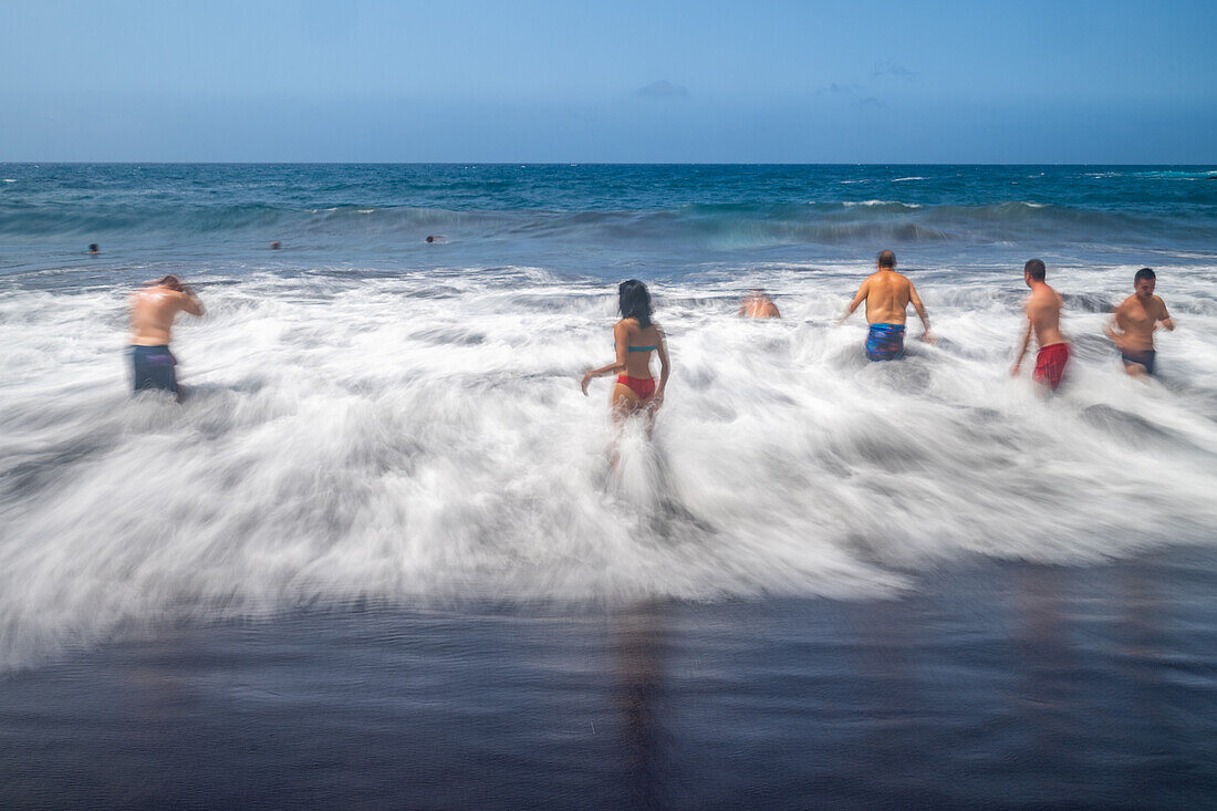 Eine Gruppe von Badenden genießt die Wellen am Bollullo-Strand an der Nordküste von Teneriffa, La Orotava, Kanarische Inseln, Spanien. Langzeitbelichtung