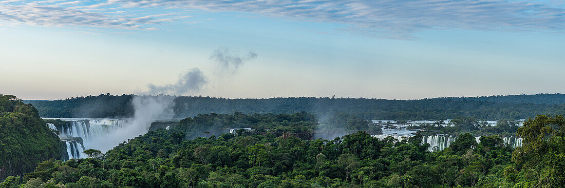 Der Iguazu-Nationalpark bei Sonnenaufgang mit einer vom Teufelsschlund aufsteigenden Nebelfahne. Der Fallkomplex erstreckt sich über eine Länge von 2,7 km, wobei die Grenze zwischen Brasilien und Argentinien durch den Teufelsschlund verläuft. Er gehört zum UNESCO-Welterbe