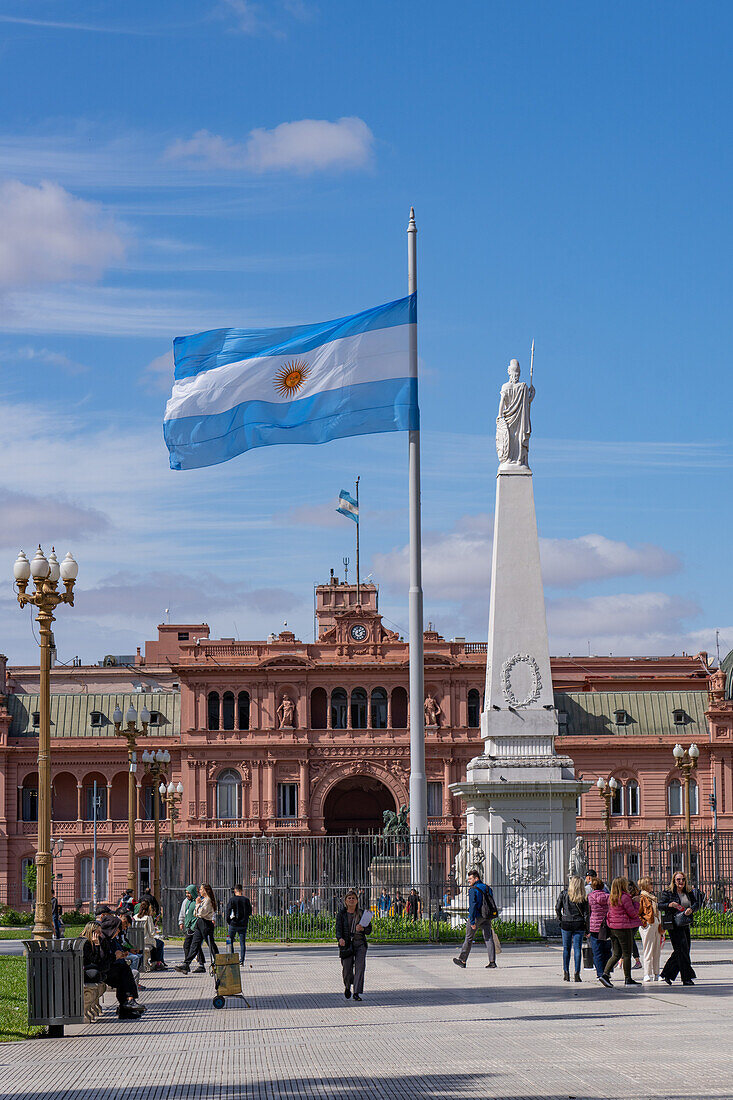 People around an Argentine flag & Pirámide de May or May Pyramid in Plaza de Mayo in front of the Casa Rosada. Buenos Aires, Argentina. The statue represents Liberty.