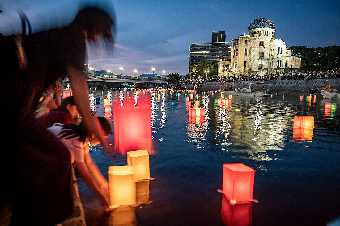 Woman and girl float lanterns on the river, in front of Atomic Bomb Dome with floating lamps on Motoyasu-gawa River during Peace Memorial Ceremony every August 6 in Hiroshima, Japan