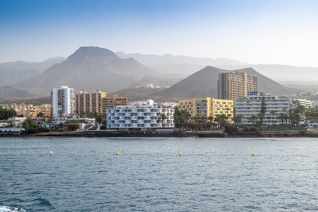 Beautiful coastal view of Los Cristianos with mountains, buildings, and the sea in Tenerife, Spain. Captured from the sea.