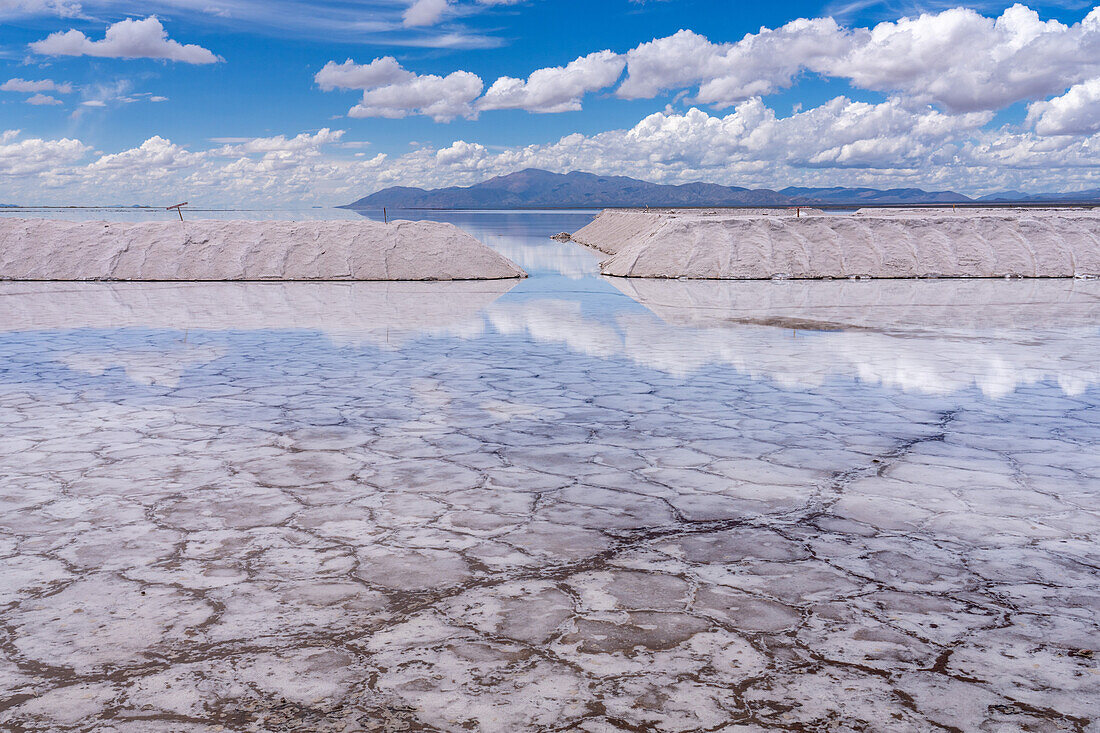 Salzhaufen in einem Salzbergwerk in den Salinen von Salinas Grandes im Nordwesten Argentiniens. Die Wolken spiegeln sich auf einer flachen Wasserfläche