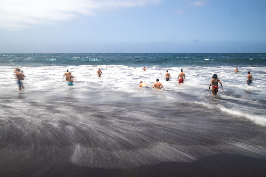 Eine Gruppe von Badegästen genießt die Wellen am Bollullo-Strand an der Nordküste von Teneriffa, La Orotava, Kanarische Inseln, Spanien. Langzeitbelichtung