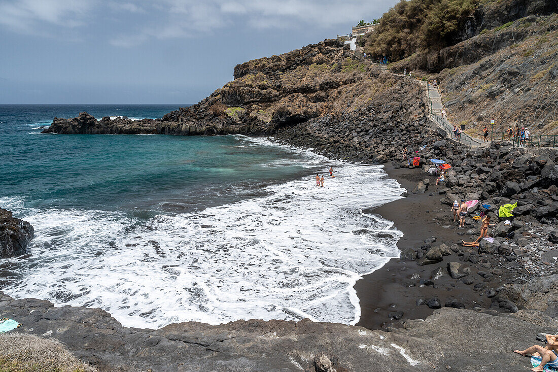 Atemberaubende Küstenansicht des Goyuyo-Strandes mit schwarzem Sand, Besuchern und blauem Meer in La Orotava, Teneriffa, Kanarische Inseln, Spanien