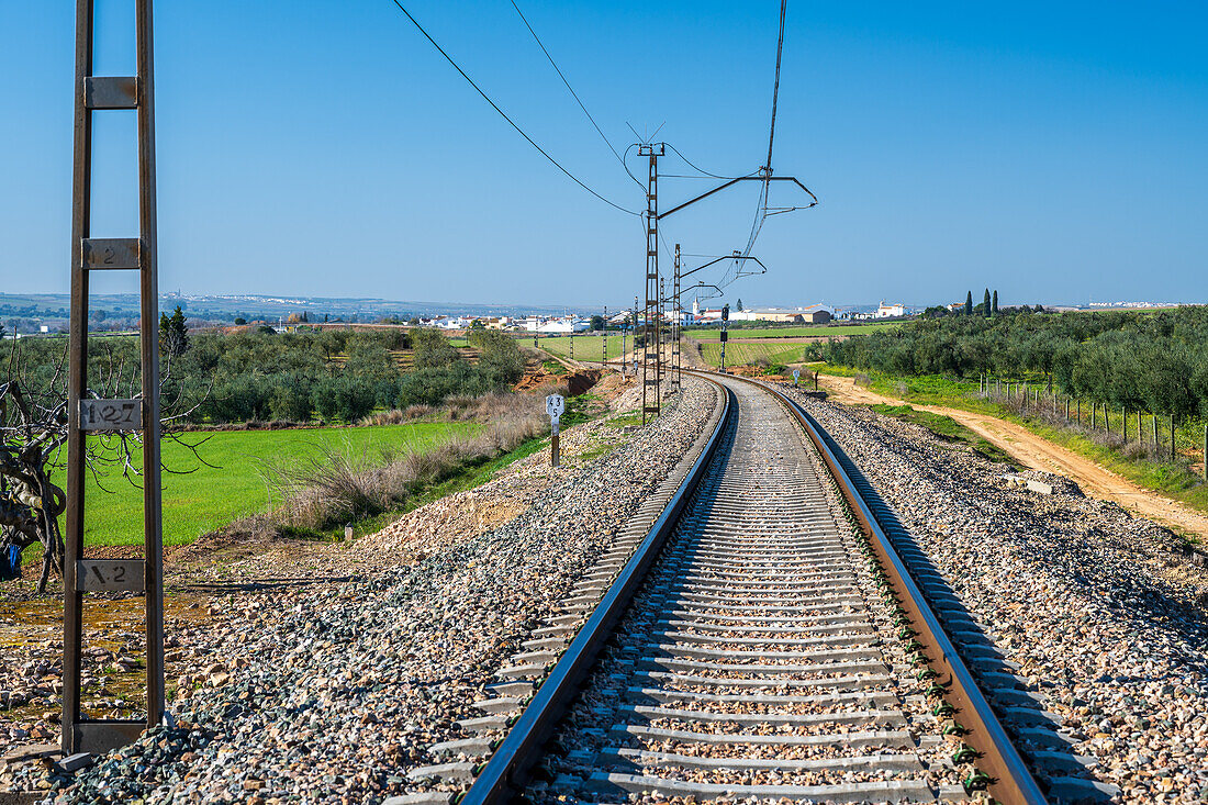 A scenic view of railway tracks cutting through the rural landscape of Carrion de los Cespedes, in Sevilla, Spain. The image captures the tranquility of the countryside.