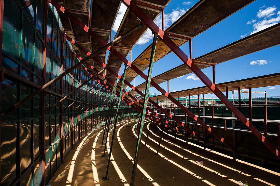 A view under empty stands of a portable bullring in Aznalcazar, Seville, Spain. The structure is highlighted by shadows and sunlight, creating a geometric pattern.