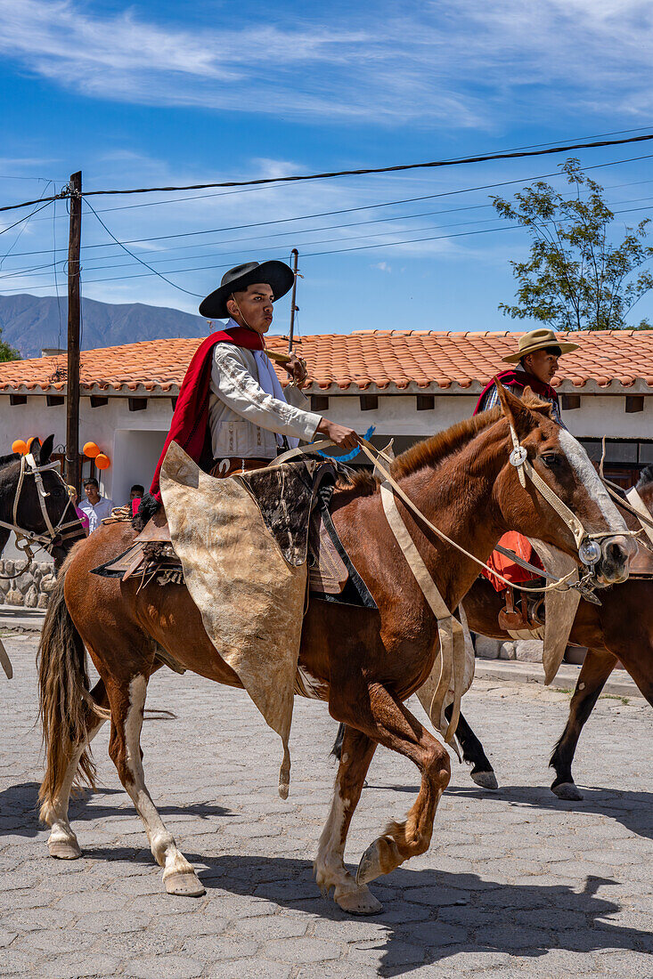 Gauchos in traditional outfits riding on horseback in a parade in Cachi, Argentina. Cowhide guardemontes protect the rider from thorn bushes common in the area.