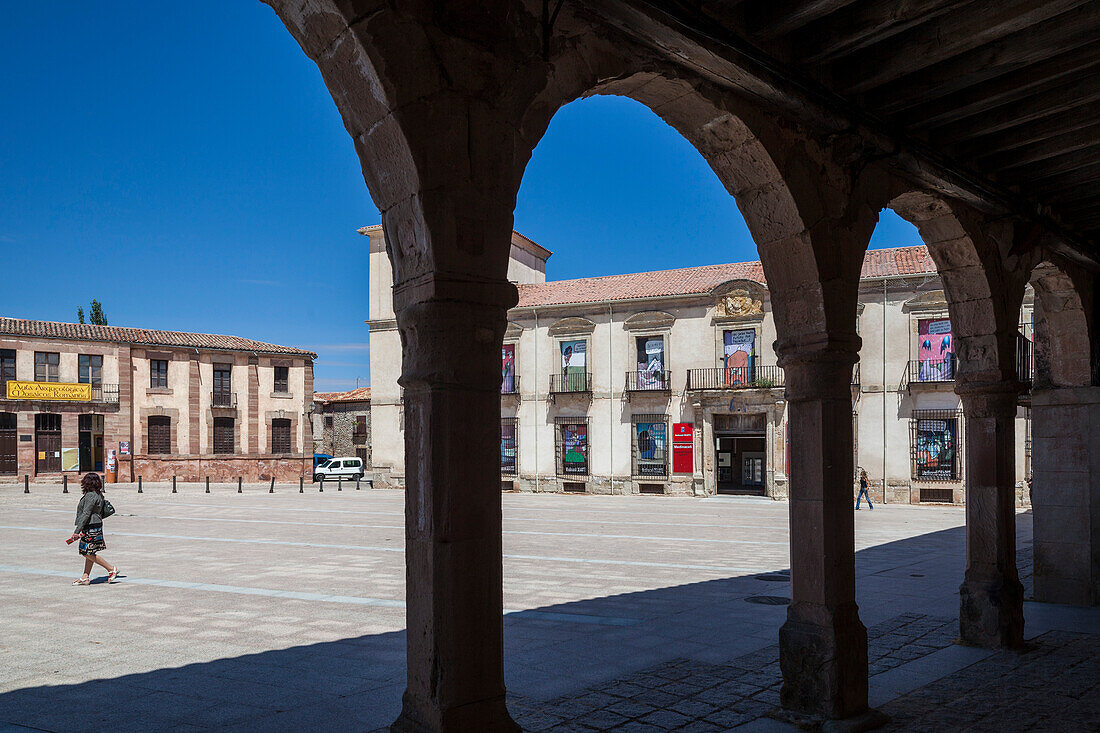 Visitors stroll through Medinaceli\'s Main Square, admiring the Ducal Palace\'s architecture under a clear blue sky.