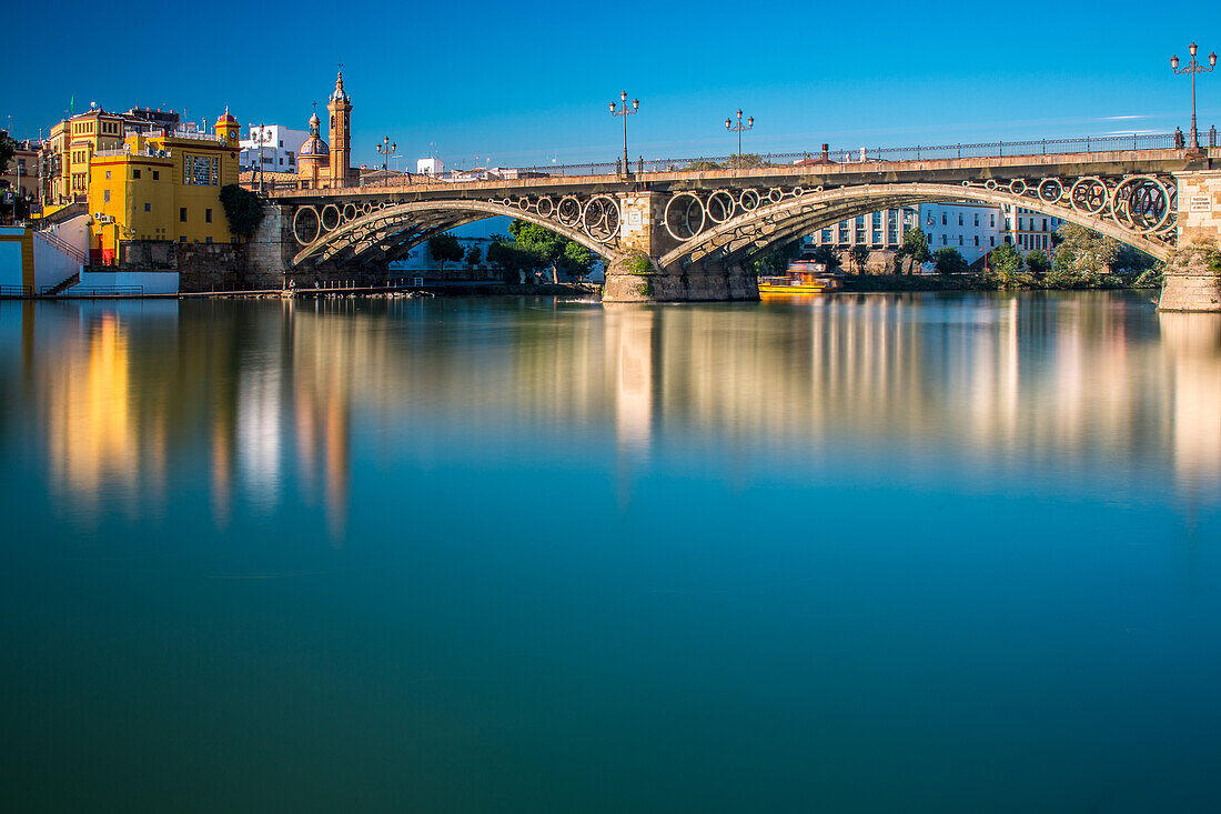 Atemberaubende Langzeitbelichtung der Triana-Brücke in Sevilla, Andalusien, mit schönen Spiegelungen auf dem Wasser und historischer Architektur bei Tageslicht