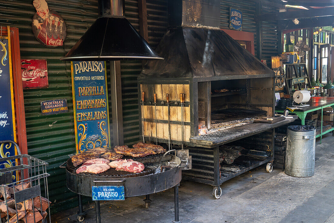 Fleisch, das über Kohlen in einem holzbefeuerten Grill in der Außenküche einer Parrilla in Caminito, La Boca, Buenos Aires, Argentinien, gegart wird