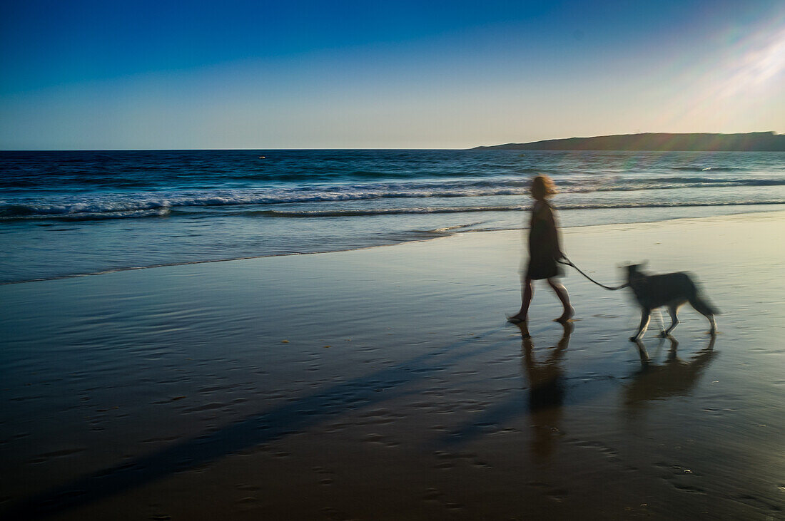 Eine Frau geht mit ihrem Hund an einem malerischen Strand bei Sonnenuntergang spazieren und fängt so ruhige und friedliche Momente in der Natur ein