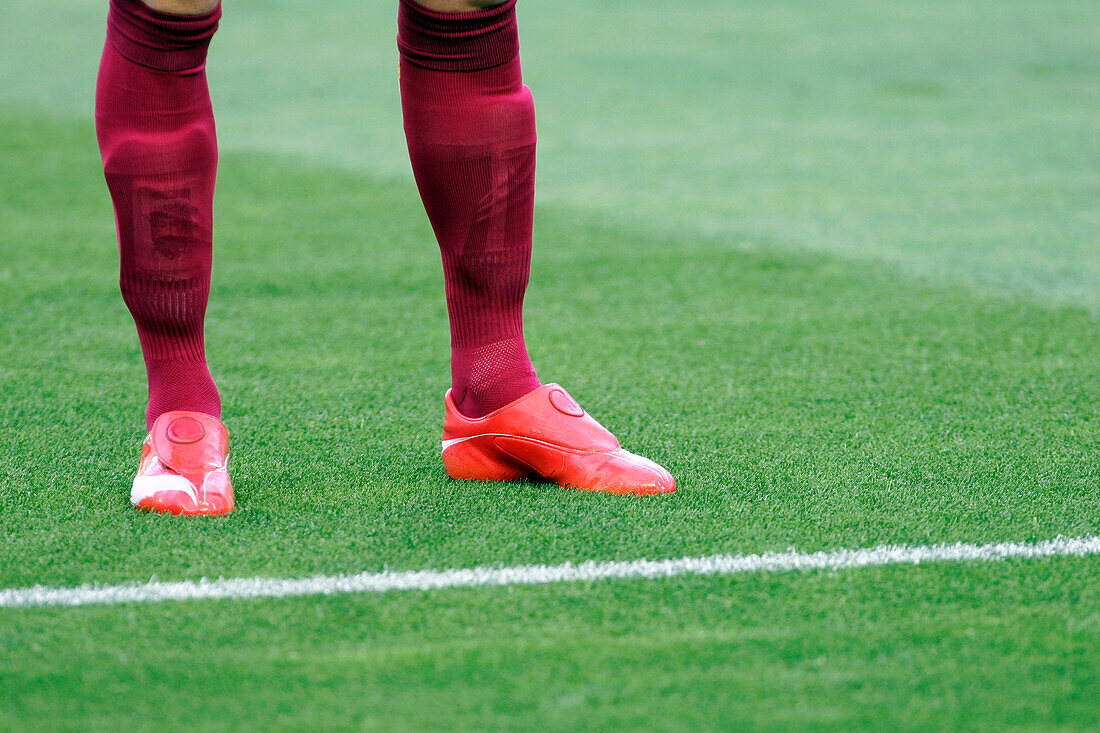 A focused image of a soccer player's red cleats and maroon socks standing on a vibrant green field. Perfect for sports and teamwork themes.