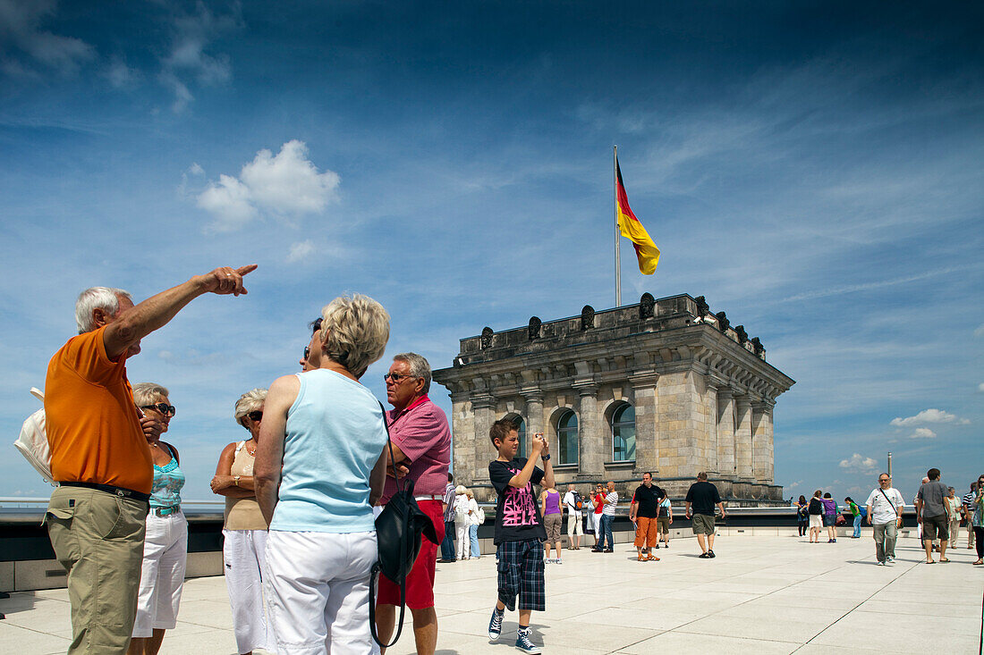 Tourists gather on the Reichstag\'s roof terrace in Berlin, admiring the cityscape and the German flag flying overhead.