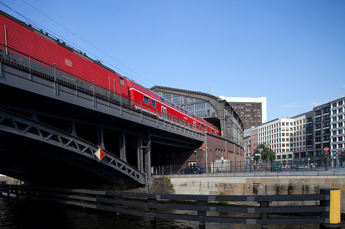 A regional train approaches Friedrichstrasse station in Berlin, showcasing the vibrant urban landscape on a clear day.