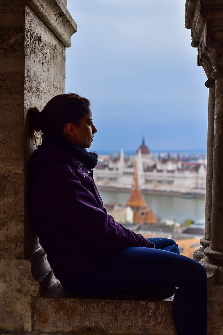 Young woman enjoying the view of Parliament building, Chain Bridge and Danube River through old columns, Budapest, Hungary, Europe