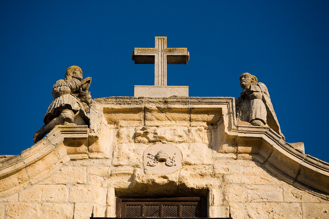 Die verzierte Spitze der Kirche Santa Cecilia mit einem Kreuz und Statuen vor einem strahlend blauen Himmel in Ronda, Andalusien