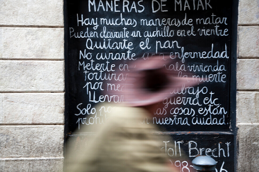 Ein Mann mit Hut schlendert an einer Wand mit Bertolt Brechts Gedicht in der Calle Tallers in Barcelona vorbei und denkt dabei über die Kunst des Ausdrucks nach