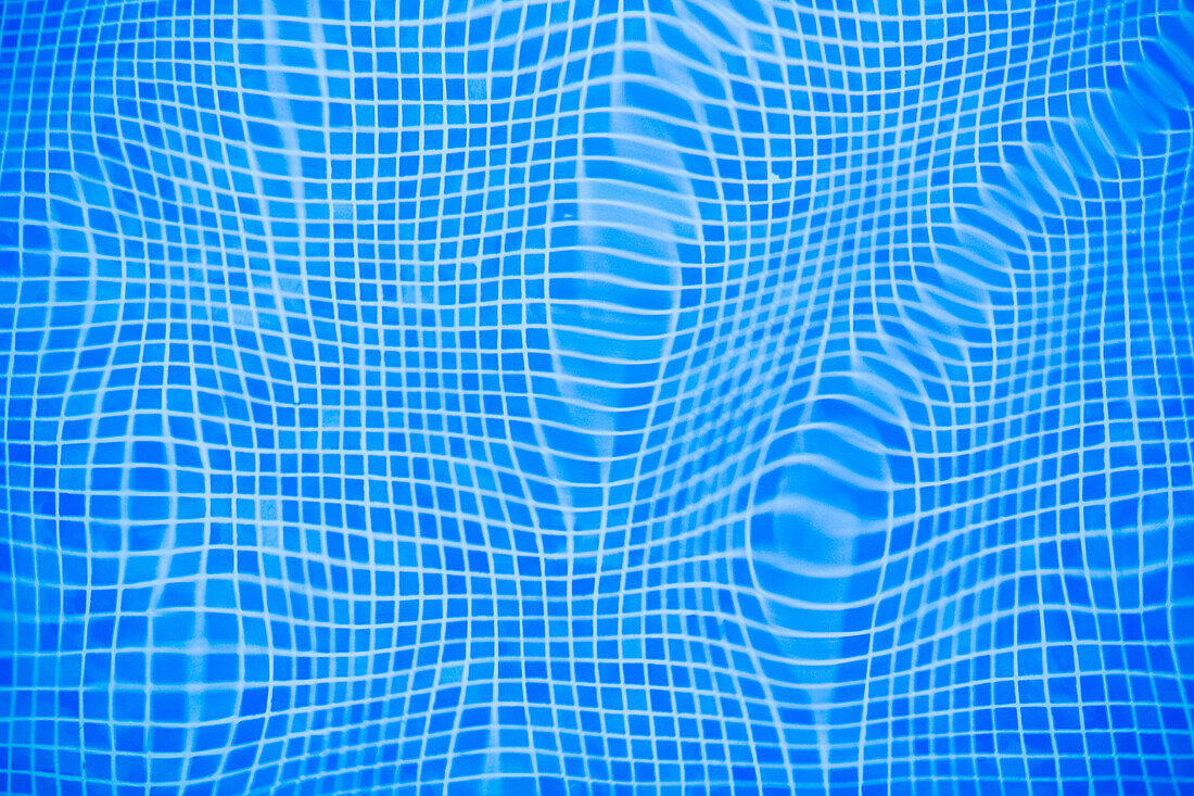 Gentle ripples and reflections create a captivating pattern in the blue tiled water of a swimming pool.